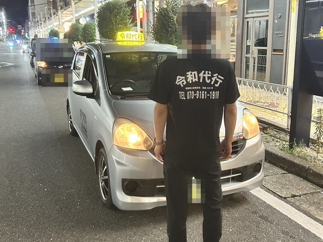 夜の通りで随伴車の前に立つ令和代行のスタッフと、後方に続く代行車両。